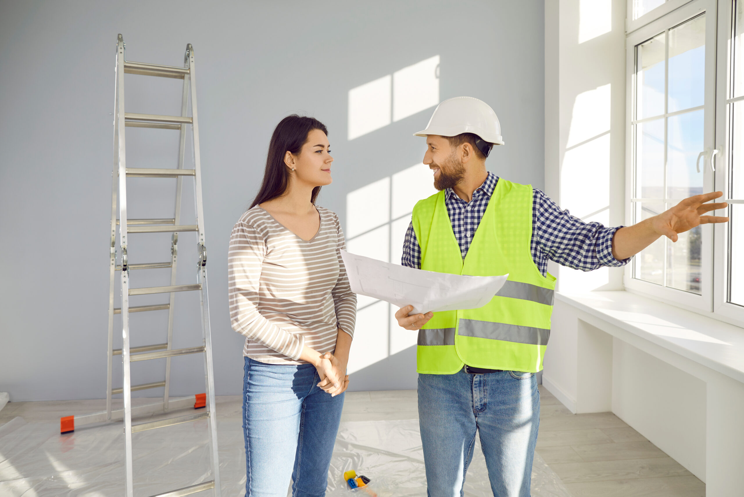 builder or construction foreman with paper plan talking to young woman house owner